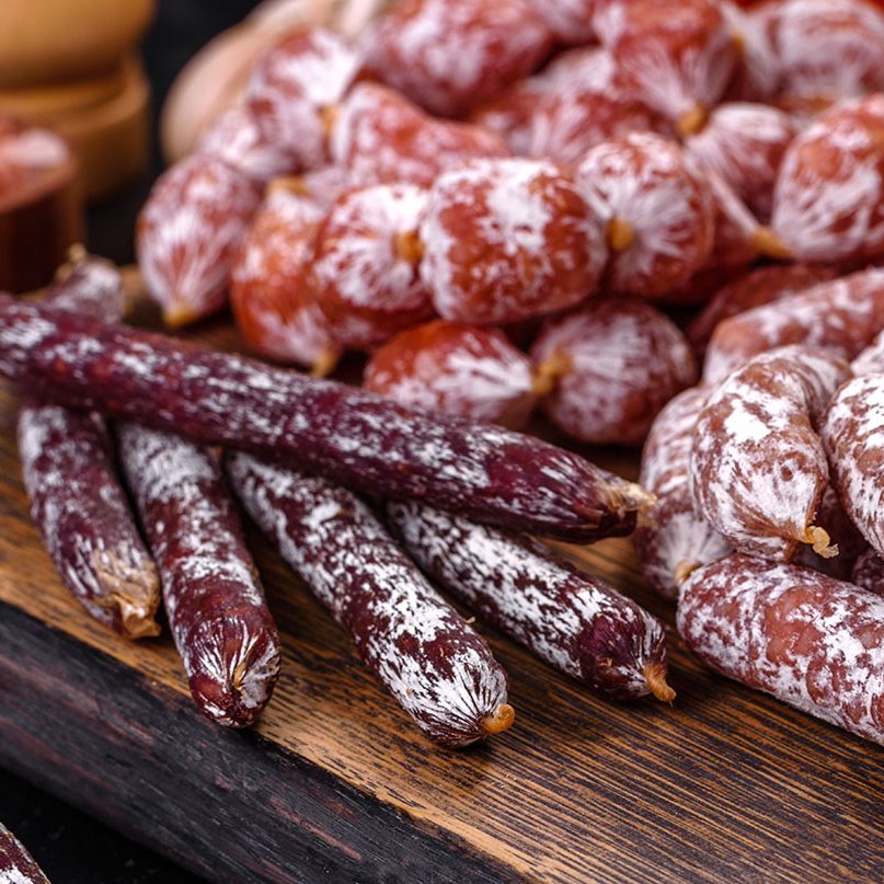 Delicious dry sausage with walnuts on a concrete table. Dry cured fuet sausage on a dark background Delicious dry sausage with walnuts on a concrete table. Dry cured fuet sausage on a dark background